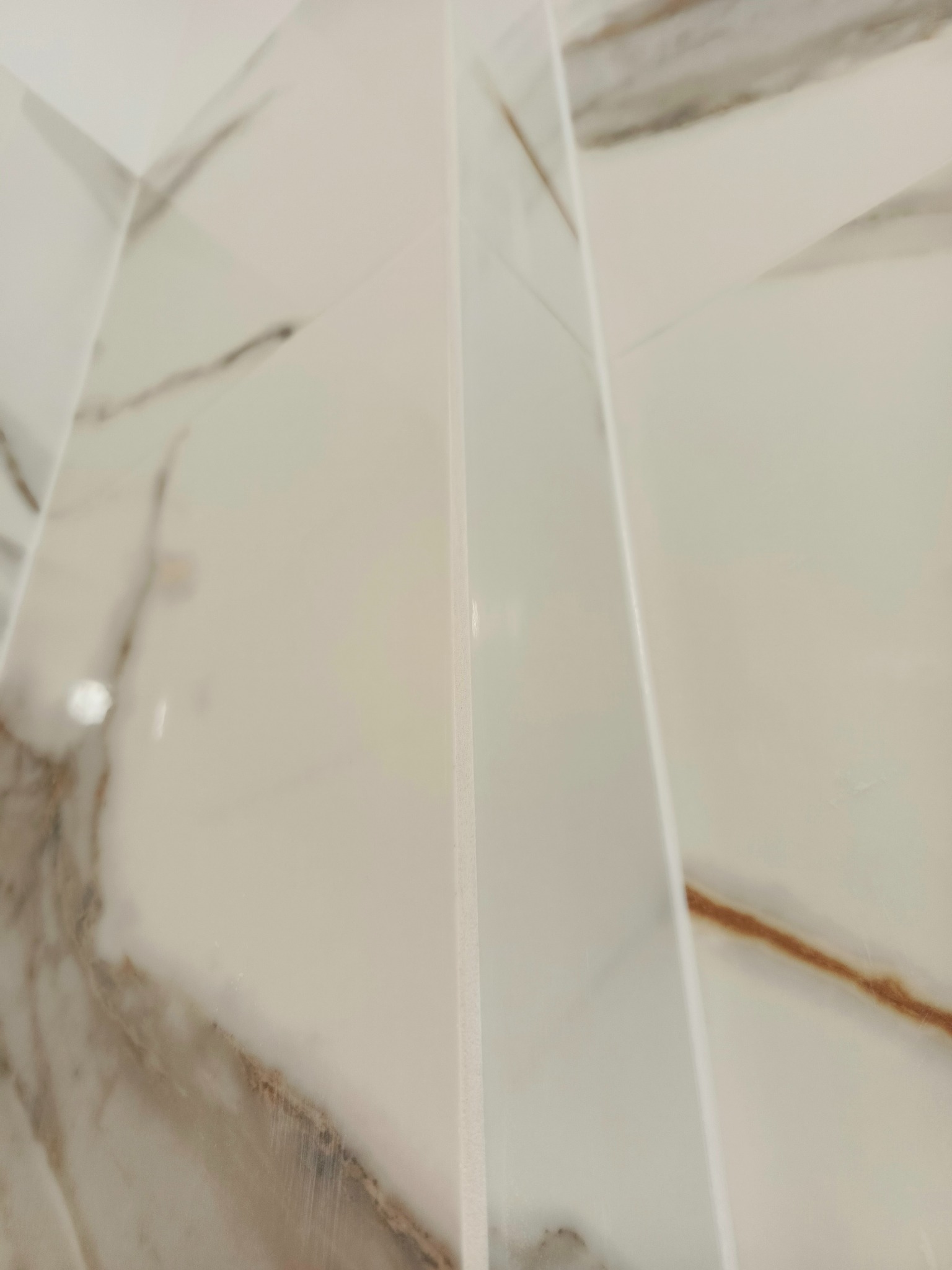 Detal wykończenia: narożnik z białych, marmurkowych płytek. Widoczne fugi i precyzja ułożenia. Nowoczesny design łazienki z bliska.