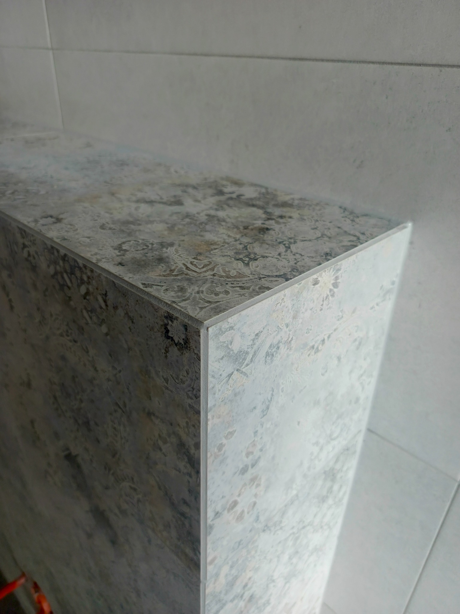 Wykończony fragment łazienki z płytkami imitującymi marmur, widok z góry na narożnik. Jasnoszara kolorystyka, minimalistyczny design.