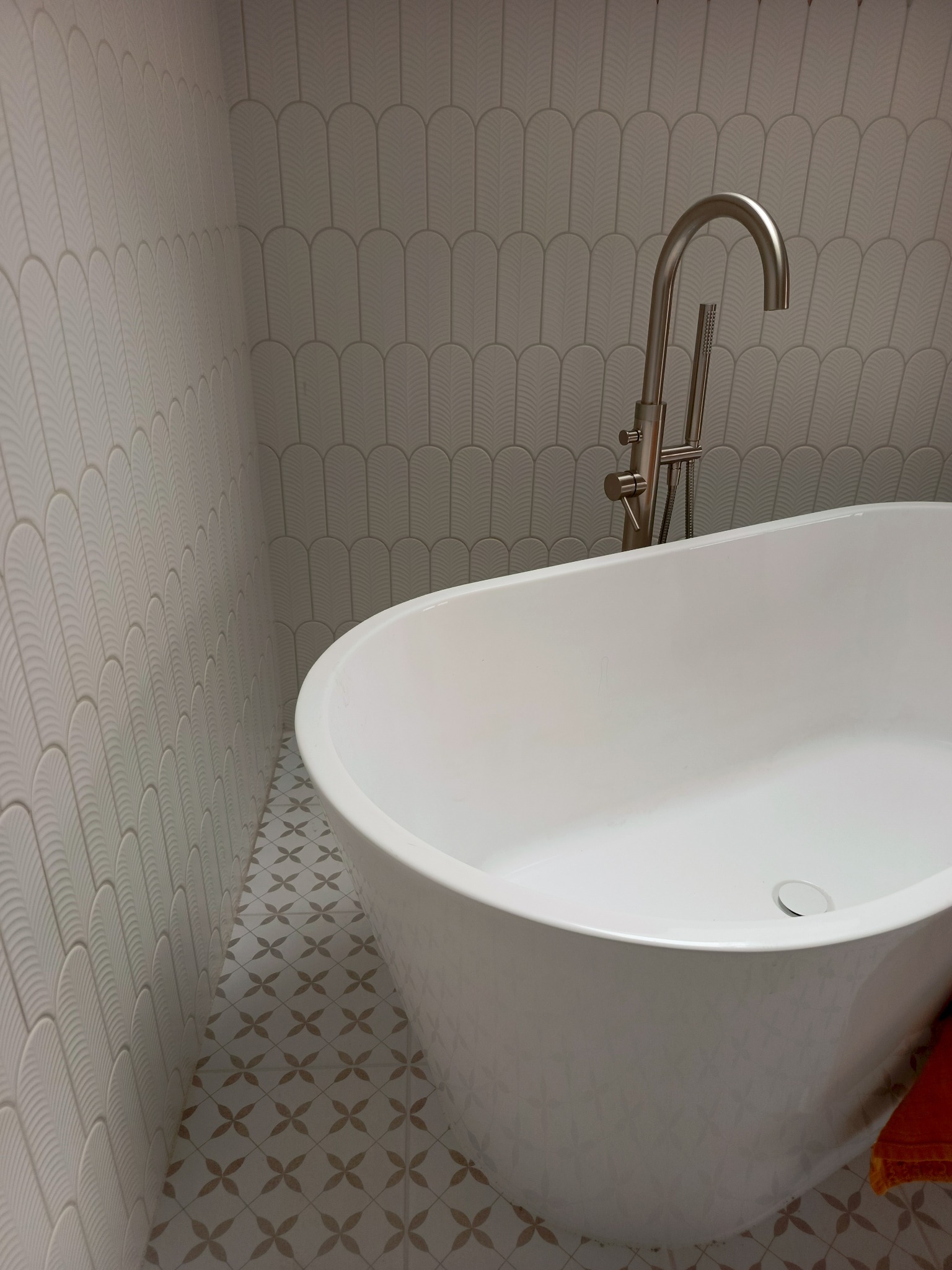 Nowoczesna łazienka z wolnostojącą wanną i armaturą w kolorze szczotkowanego niklu. Ściany i podłoga wyłożone płytkami w delikatny wzór.