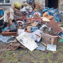 J & M SPARTA Mateusz RUTKOWSKI - Sterta odpadów i śmieci przed budynkiem w Tarnowskich Górach, widoczne worki, meble, skrzynki i inne pozostałości po remoncie lub opróżnianiu mieszkania.