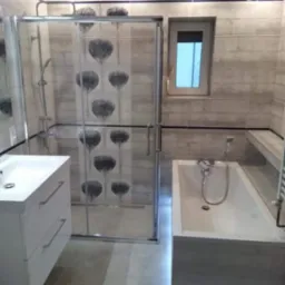 Nowoczesna łazienka z kabiną prysznicową z motywem kwiatowym na szklanych drzwiach i podświetlaną wanną, wykończona płytkami w odcieniach szarości.