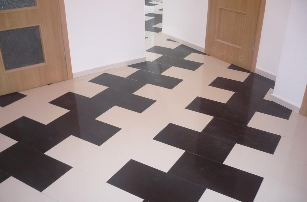 Ułożona podłoga z płytek w kształcie krzyży z ciemnego brązu i beżu, widok na korytarz z dwiema drewnianymi futrynami drzwi.