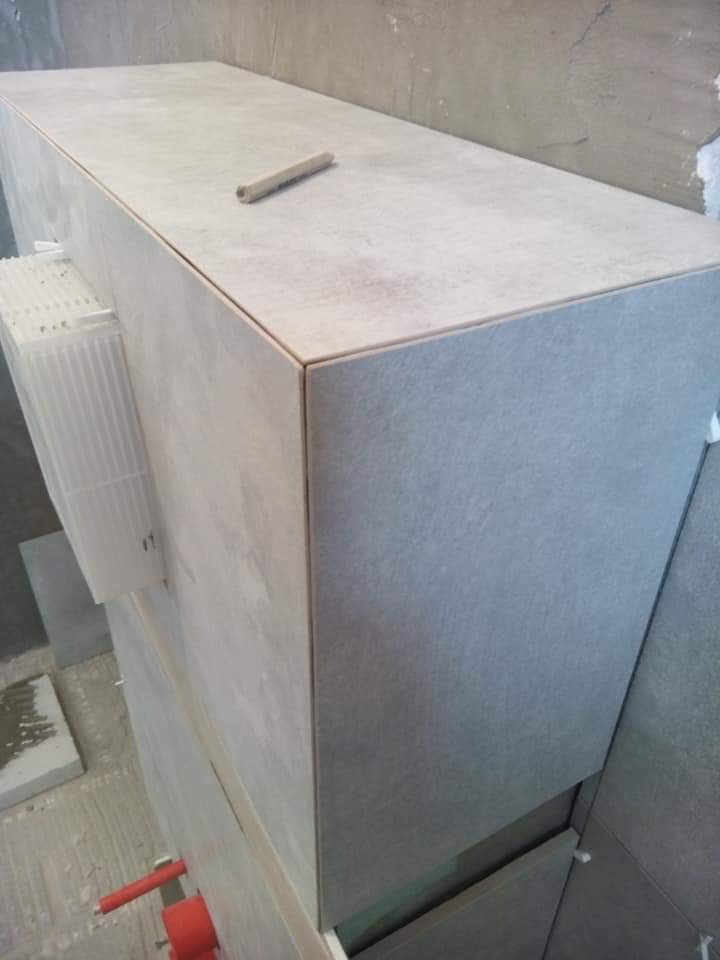 Szary zabudowany stelaż WC z płytek ceramicznych w trakcie montażu, z użyciem krzyżyków dystansowych i poziomicy na górnej powierzchni.