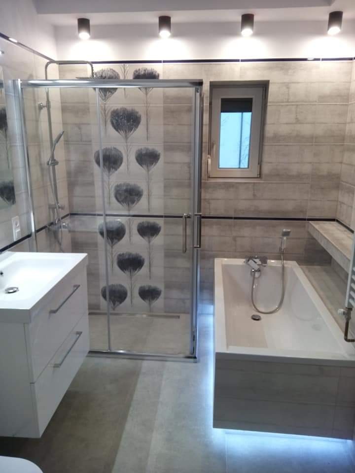 Nowoczesna łazienka z kabiną prysznicową z motywem kwiatowym na szklanych drzwiach i podświetlaną wanną, wykończona płytkami w odcieniach szarości.