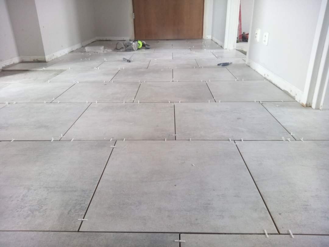 Układanie szarych, kwadratowych płytek podłogowych z użyciem krzyżyków dystansowych w trakcie prac wykończeniowych.