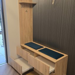 SEBEX Sebastian Chojnacki - Funkcjonalna szafka z siedziskiem i wieszakami w przedpokoju, wykończona w odcieniach drewna, z otwartymi szufladami i ciemnymi poduszkami siedziskowymi.