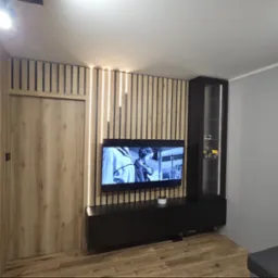 Nowoczesna aranżacja salonu z drewnianą ścianą z lameli i podświetleniem LED, czarna szafka RTV z telewizorem i witryna z oświetleniem wewnętrznym.