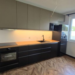 SEBEX Sebastian Chojnacki - Nowoczesna kuchnia z szarymi szafkami górnymi i czarnymi dolnymi, drewnianym blatem, czarną armaturą i wzorzystą podłogą. Widok na okno z widokiem na zieleń.