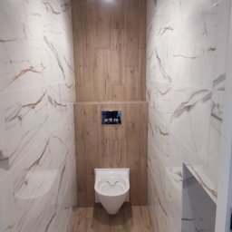 Marek Podstawka - Nowoczesna toaleta w beżowo-białej kolorystyce, z płytkami imitującymi marmur i drewno. Podwieszana miska WC i minimalistyczny przycisk spłukujący.