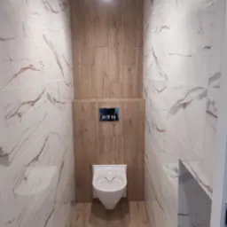 Nowoczesna toaleta w beżowo-białej kolorystyce, z płytkami imitującymi marmur i drewno. Podwieszana miska WC i minimalistyczny przycisk spłukujący.