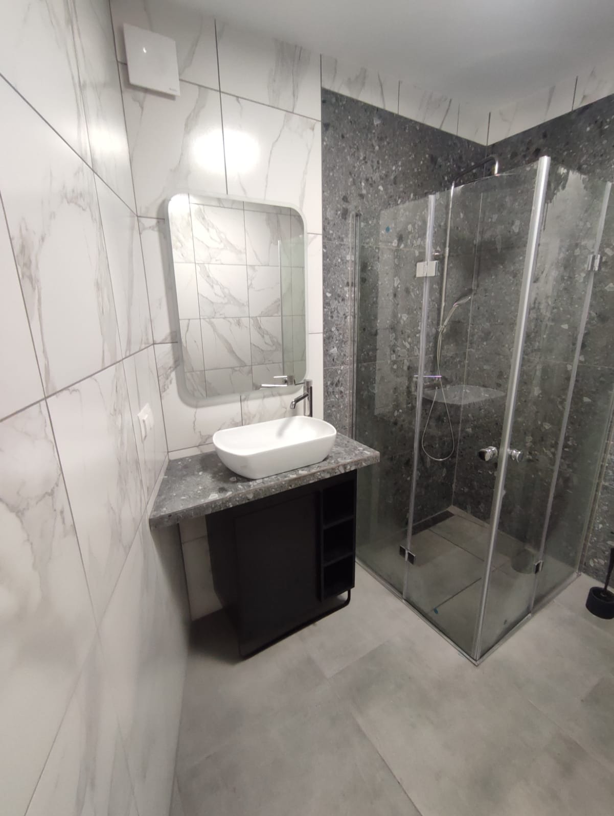 Nowoczesna łazienka z kabiną prysznicową i umywalką nablatową, wykończona płytkami imitującymi marmur i szarym lastryko.