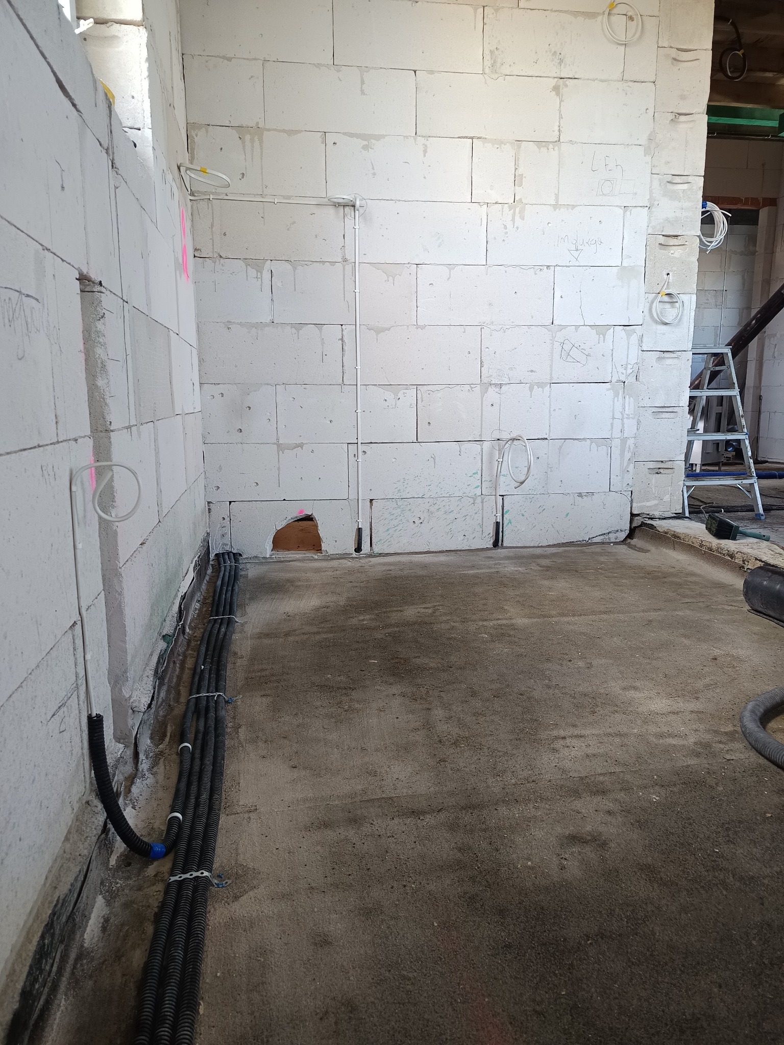 Wnętrze w trakcie prac instalacyjnych: kable w peszlach ułożone wzdłuż ściany z betonu komórkowego, widoczne punkty wyprowadzenia przewodów elektrycznych.