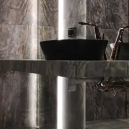 Nowoczesna łazienka z marmurowymi ścianami, czarną umywalką nablatową i złotą armaturą, oświetlona pionowymi pasami LED.