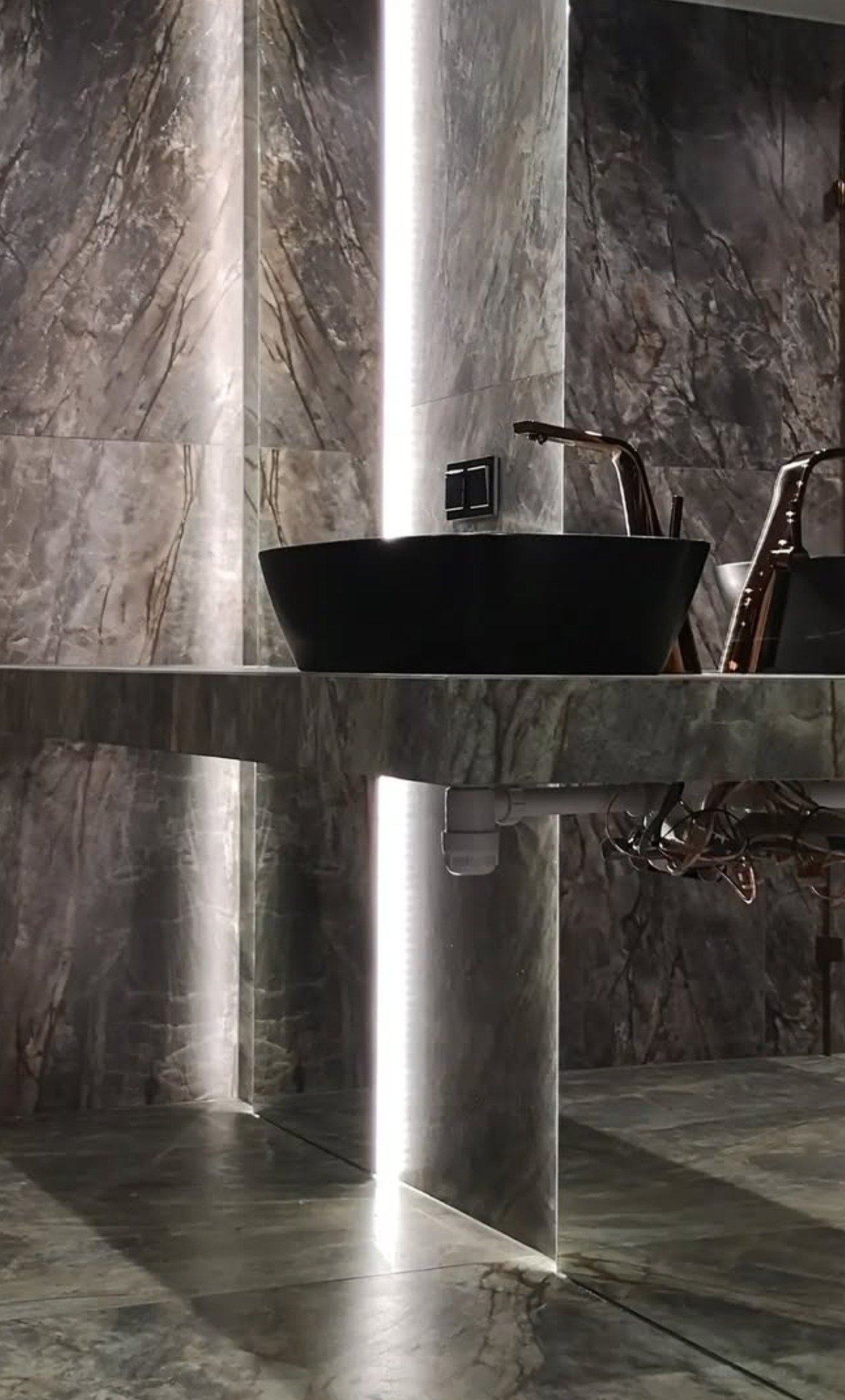 Nowoczesna łazienka z marmurowymi ścianami, czarną umywalką nablatową i złotą armaturą, oświetlona pionowymi pasami LED.