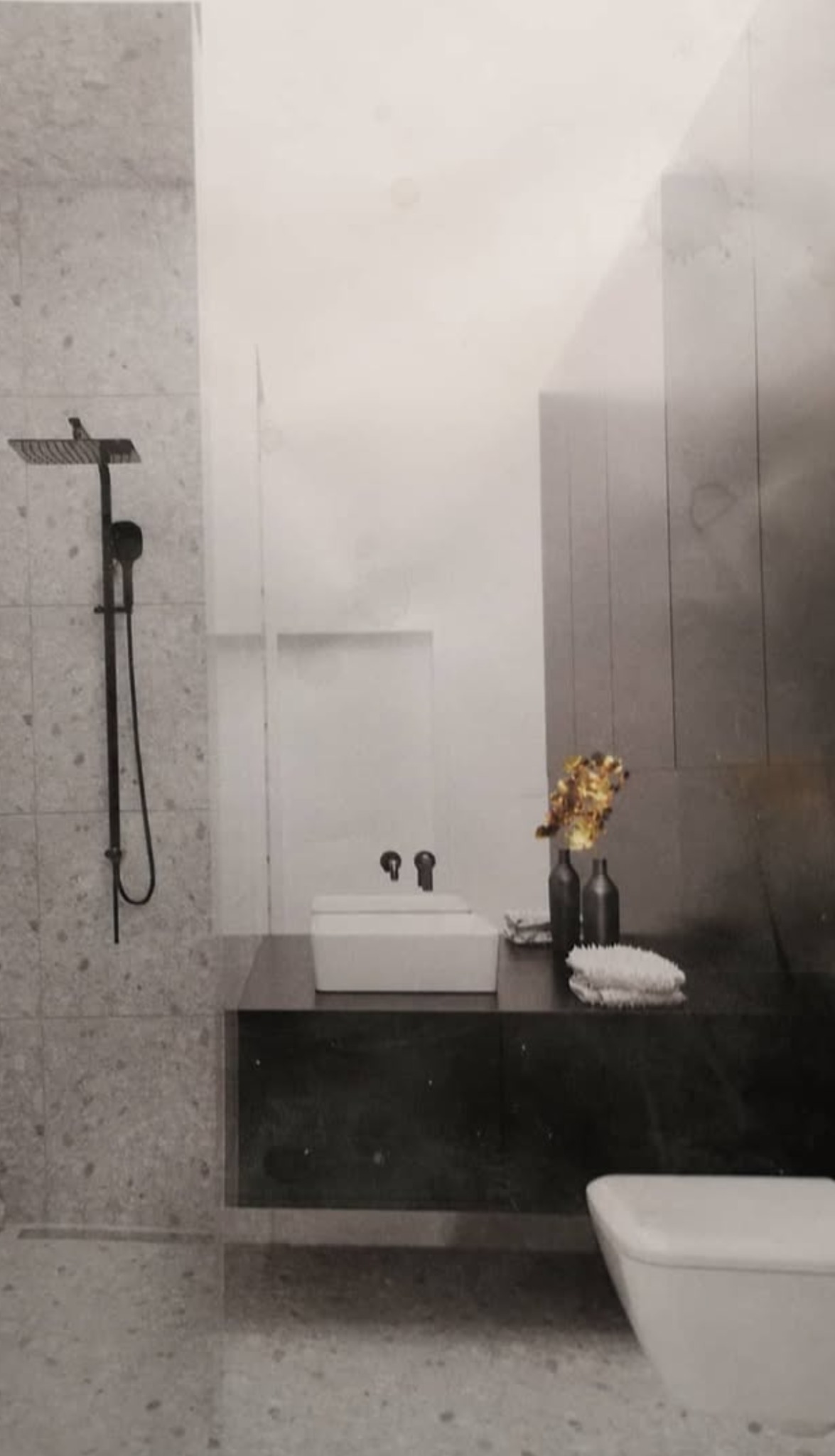 Nowoczesna łazienka w odcieniach szarości z czarną armaturą, deszczownicą i umywalką nablatową, dekorowana suszonymi kwiatami w ciemnych wazonach.