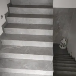 Wykończone schody z szarych płytek imitujących marmur, z dekoracyjną latarenką na podeście. Widok z góry, podkreślający wzór i precyzję ułożenia płytek.