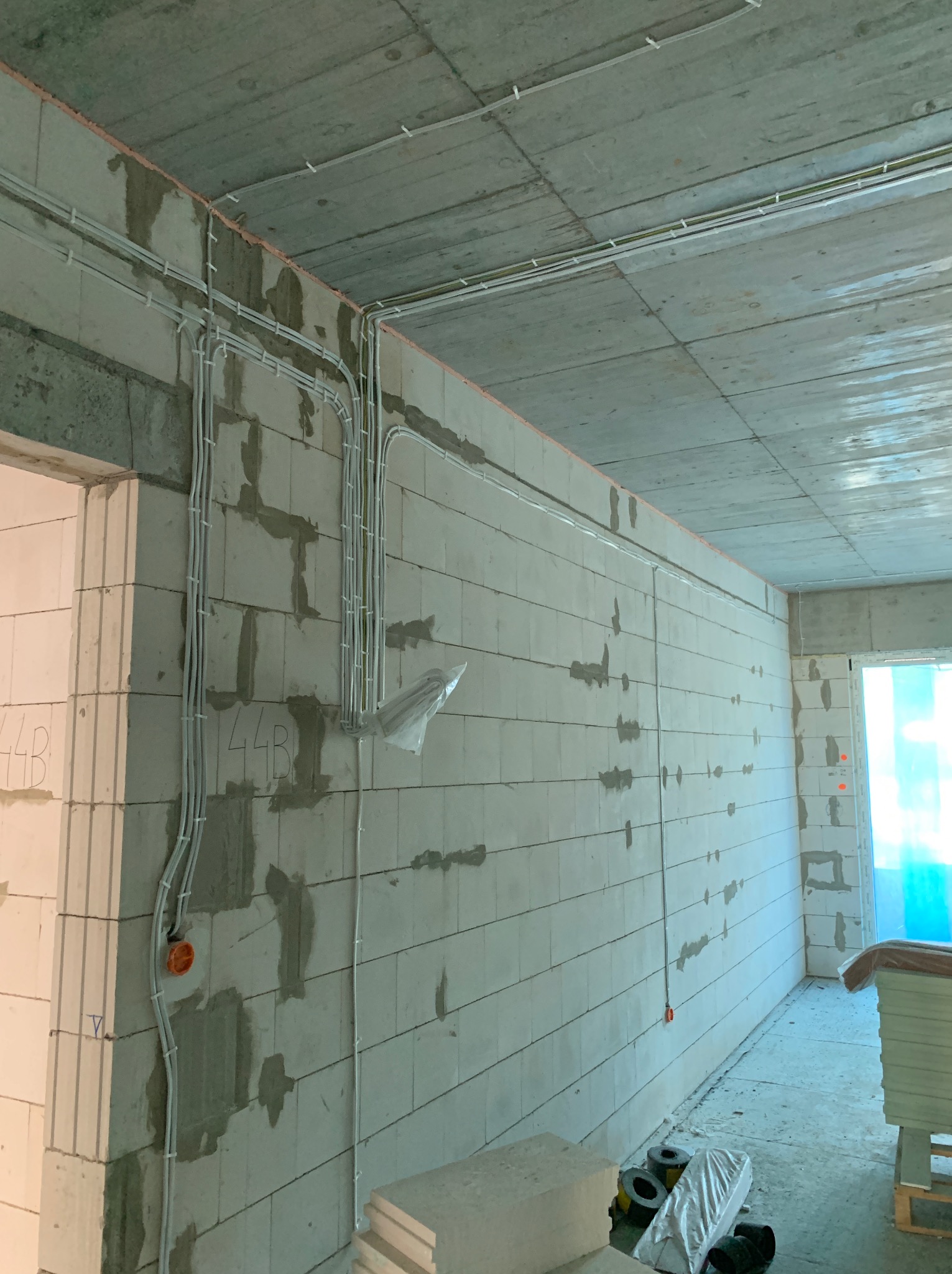 Surowy stan wnętrza z widocznymi przewodami elektrycznymi zamocowanymi do surowych ścian z betonu komórkowego, widoczne puszki instalacyjne i kable prowadzone po ścianach i suficie.