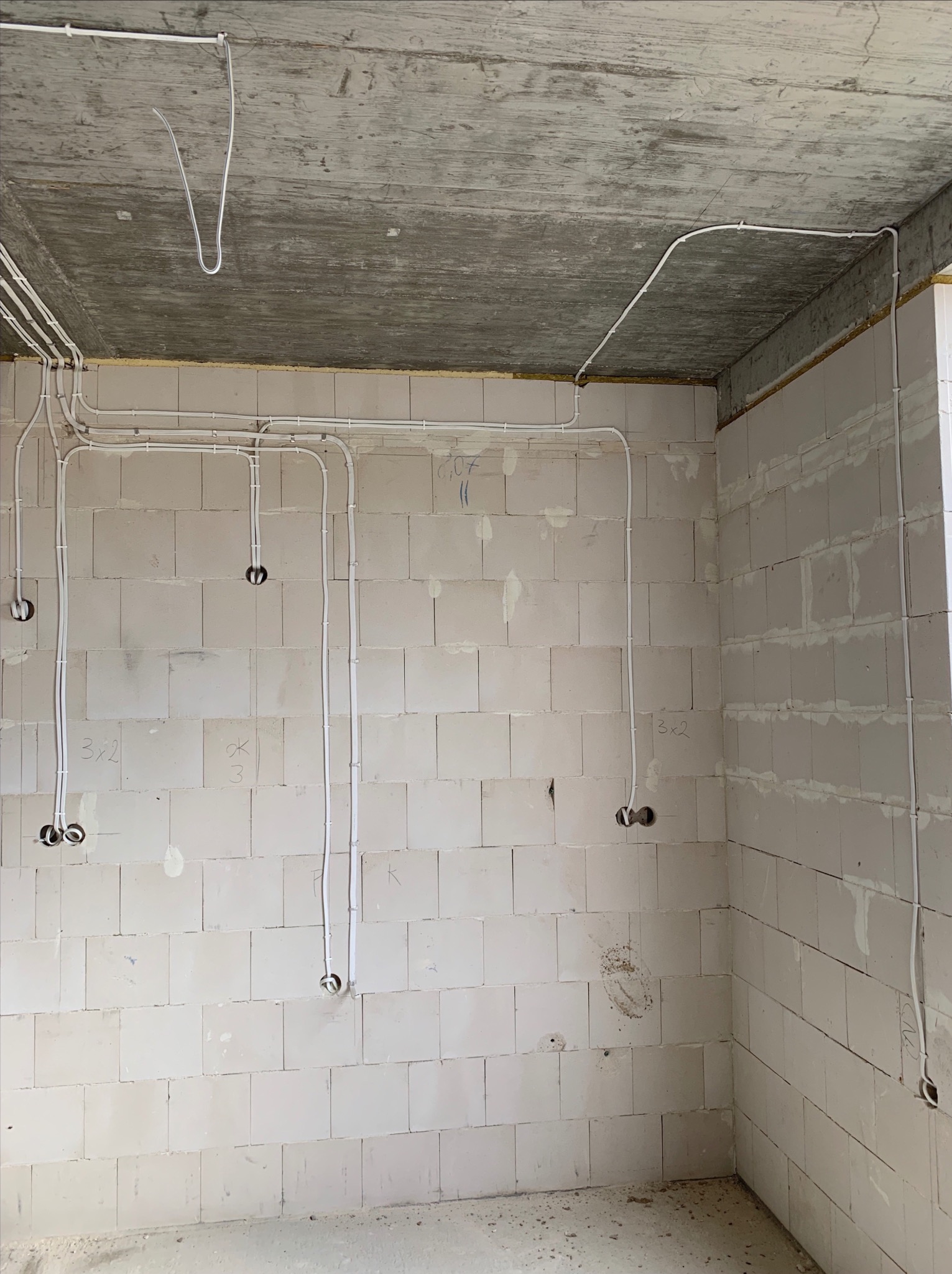 Surowy stan wnętrza z widocznymi przewodami elektrycznymi prowadzonymi po ścianach z betonu komórkowego i suficie, przygotowanymi pod gniazdka i oświetlenie.