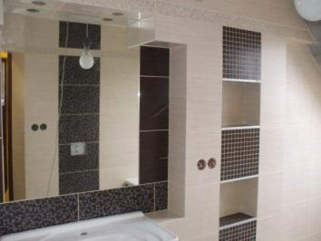 Beżowo-brązowa łazienka z lustrem i półkami wyłożonymi mozaiką, widoczne fragmenty umywalki i oświetlenia, świeżo po malowaniu.