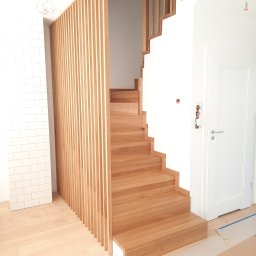 DOMAR STOLARSTWO - Jasne drewniane schody z ażurową balustradą z pionowych listew, widoczne zabezpieczenia podłogi. Minimalistyczny design, naturalne światło, nowoczesne wykończenie wnętrza.