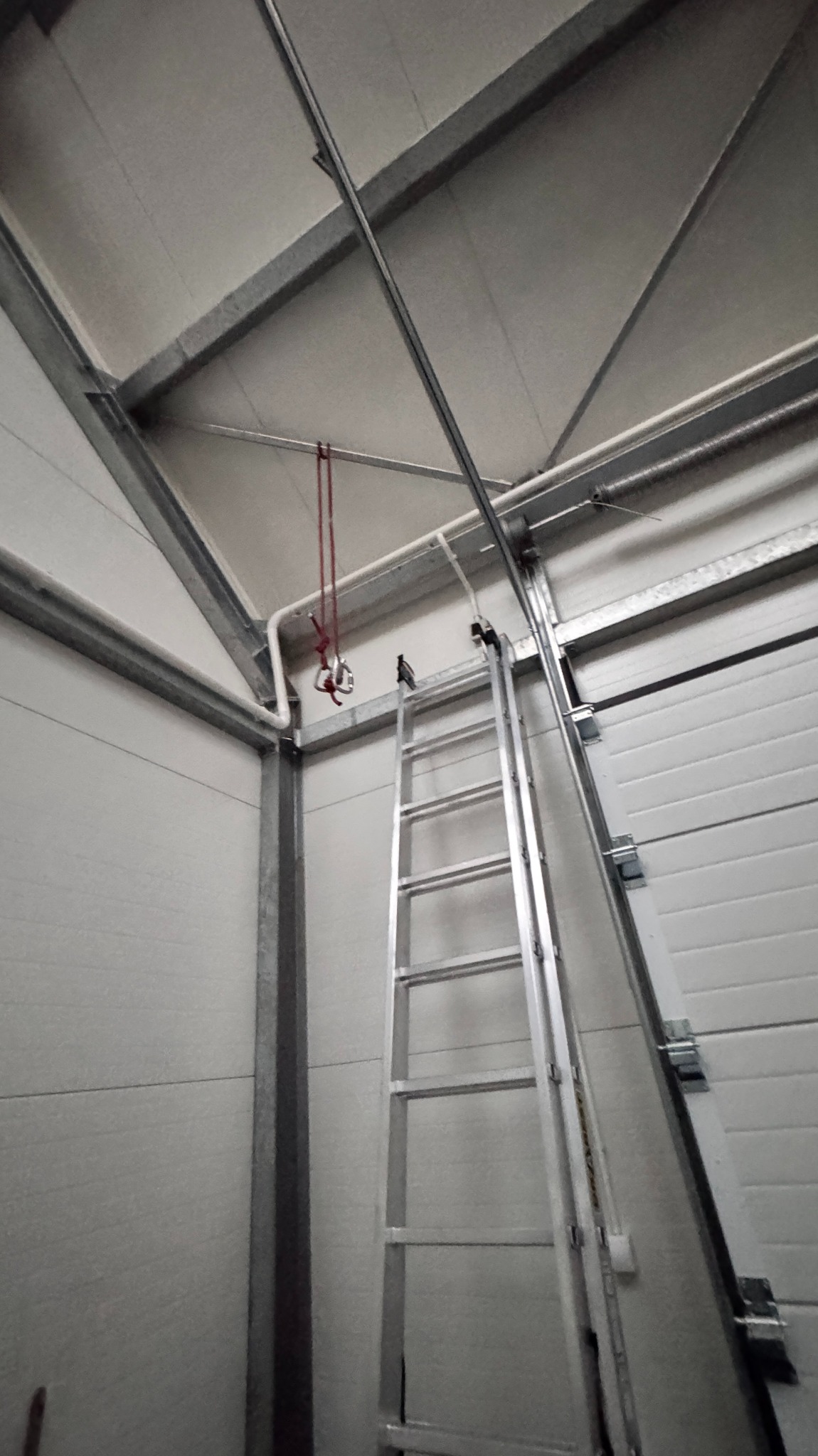 Wnętrze hali w trakcie montażu wentylacji: drabina oparta o ścianę, widoczne elementy konstrukcyjne i instalacyjne. Ujęcie z dołu, oświetlenie surowe.