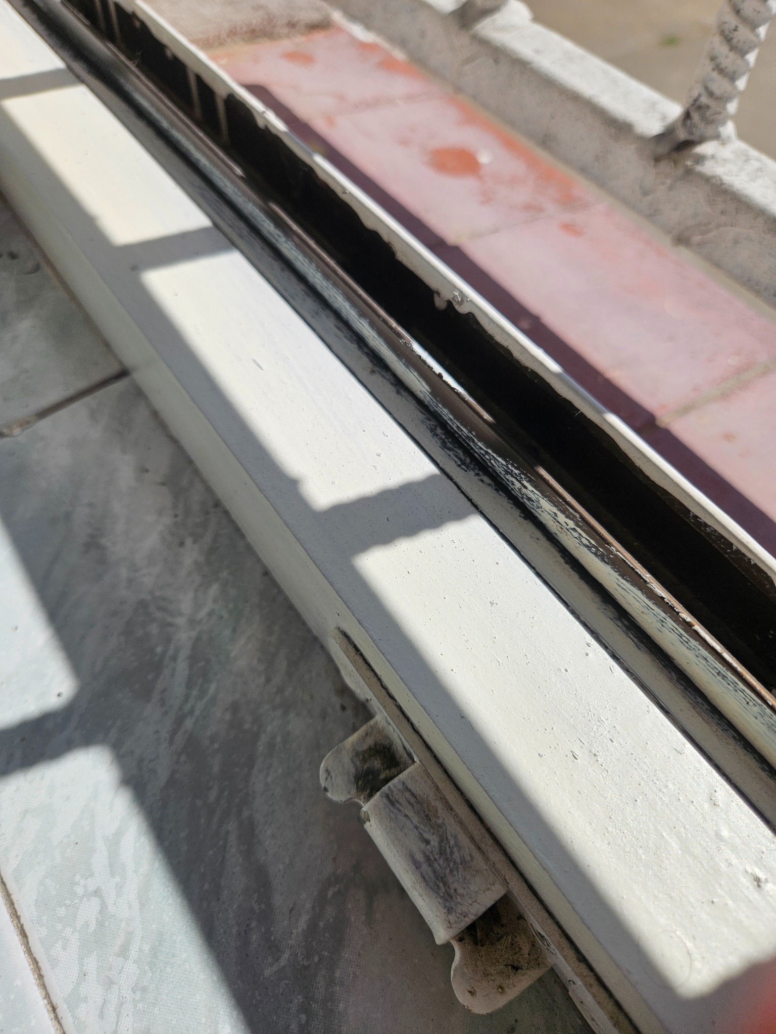 Brudna, biała rama okienna z widocznymi zabrudzeniami w prowadnicach. Szczegółowe ujęcie na zanieczyszczenia w rowkach okna.