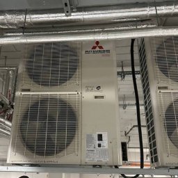 AGDKlinika - Białe, przemysłowe klimatyzatory Mitsubishi Heavy Industries LTD zamontowane pod sufitem w pomieszczeniu. Widoczne rury wentylacyjne.