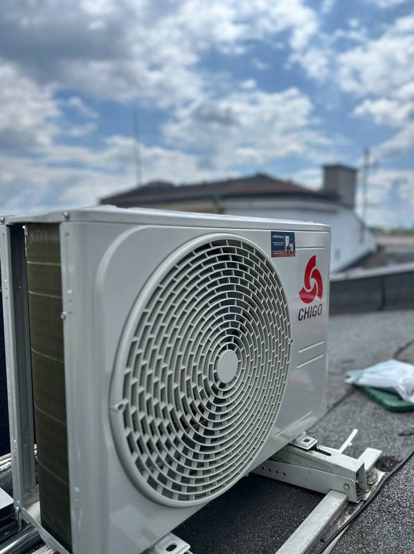 Zamontowana jednostka zewnętrzna klimatyzacji Chigo na dachu budynku z widocznym niebem i fragmentem dachu innego budynku w tle. Kątowe ujęcie z bliska.
