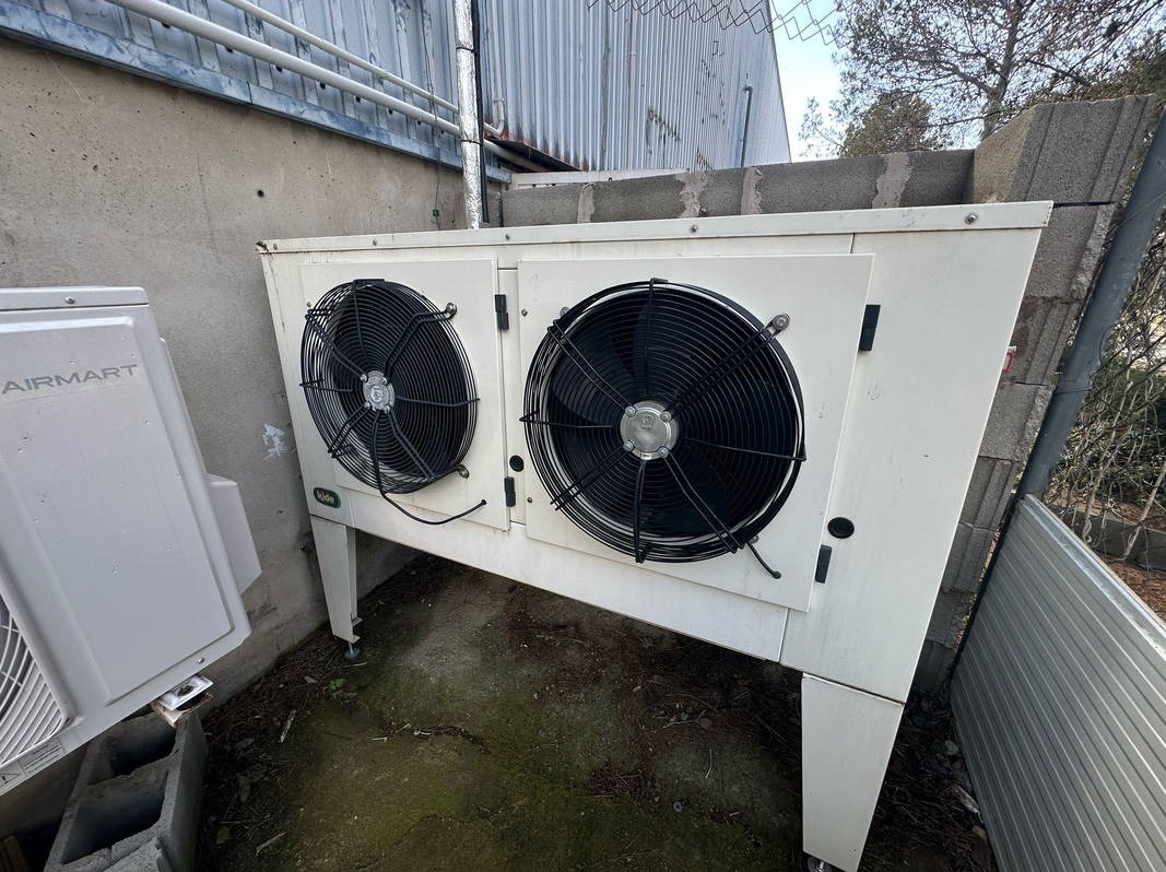 Dwa wentylatory klimatyzacyjne na zewnątrz budynku, obok jednostki AirMart. Widoczne przewody i elementy konstrukcyjne. Ujęcie z dołu, perspektywa zniekształcona.