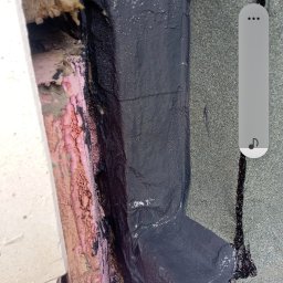 Dachy Płaskie Dawid Karpiak - Szczegółowe ujęcie naprawy dachu z użyciem czarnej masy uszczelniającej, widoczne materiały izolacyjne i fragment pokrycia dachowego.