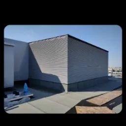 Nowoczesne krycie dachu blachą trapezową na budynku. Widoczne elementy izolacji i obróbki blacharskiej. Dach płaski z widokiem na miasto w tle.