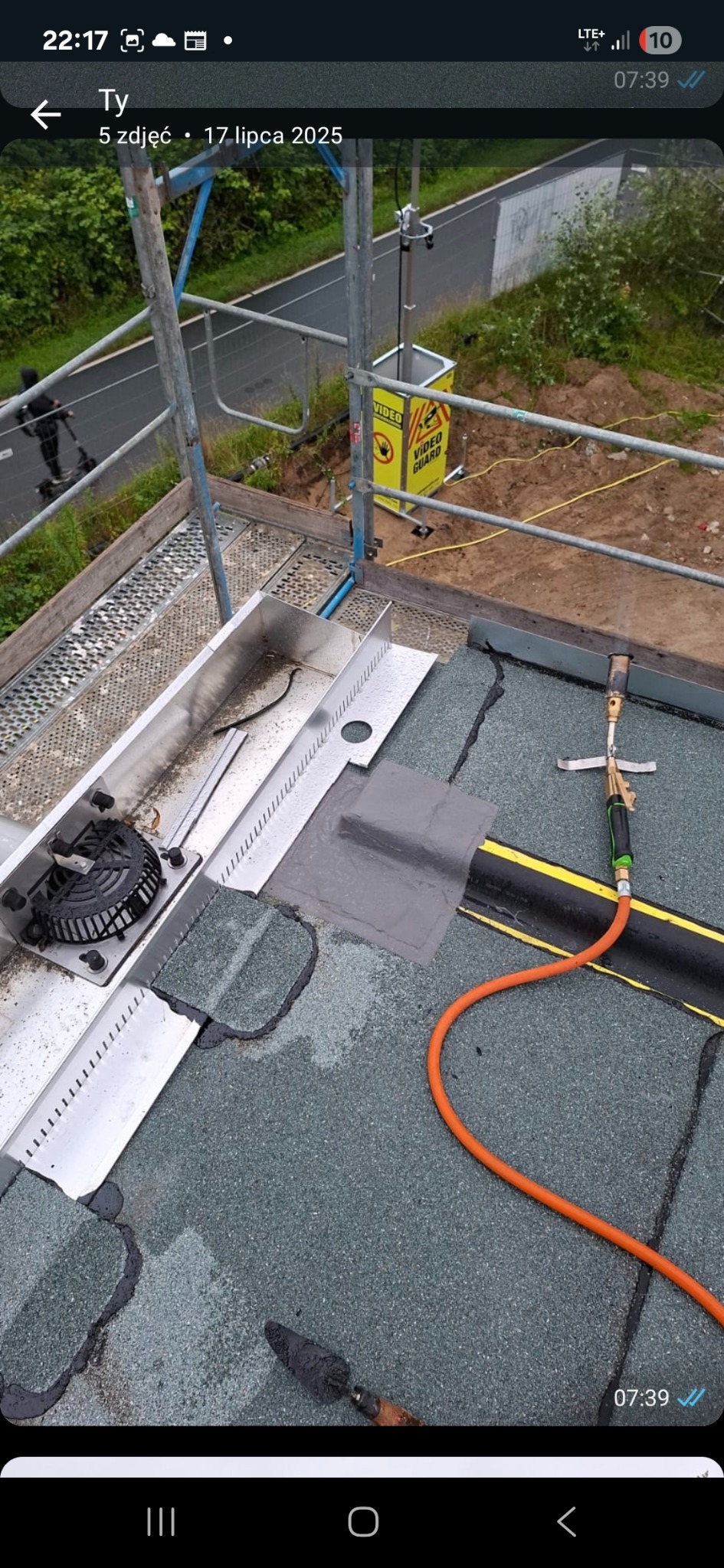 Naprawa dachu z użyciem palnika dekarskiego i łaty bitumicznej. Widoczny fragment rynny. Prace dekarskie na płaskim dachu z papy.