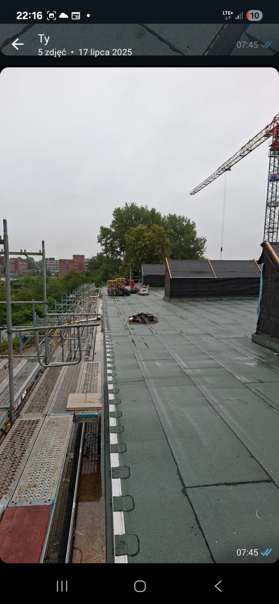 Zielony dach pokryty papą termozgrzewalną w trakcie prac dekarskich. Widoczne rusztowania, materiały budowlane i dźwig w tle. Prace dekarskie w toku.