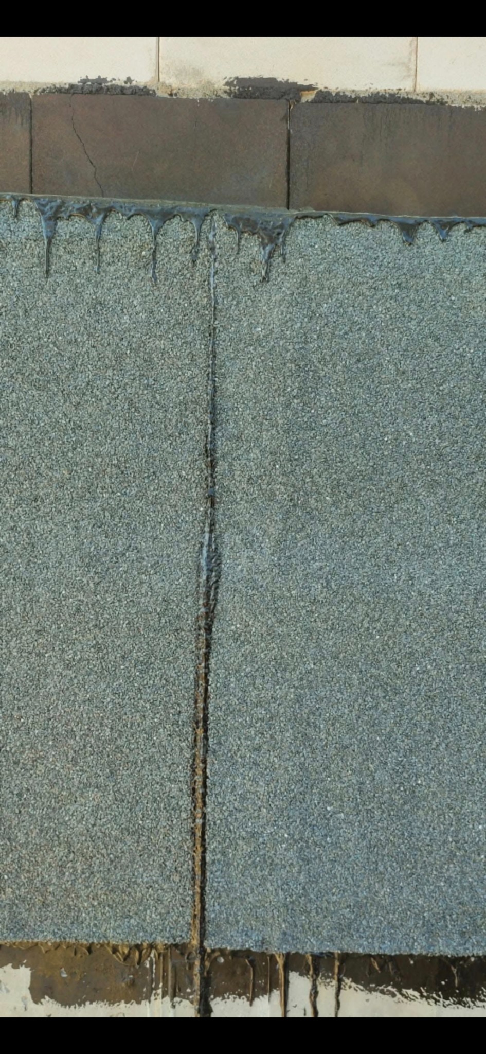 Zbliżenie na fragment dachu pokrytego papą z widocznymi spoinami i śladami smoły. Ukazane detale hydroizolacji dachu.