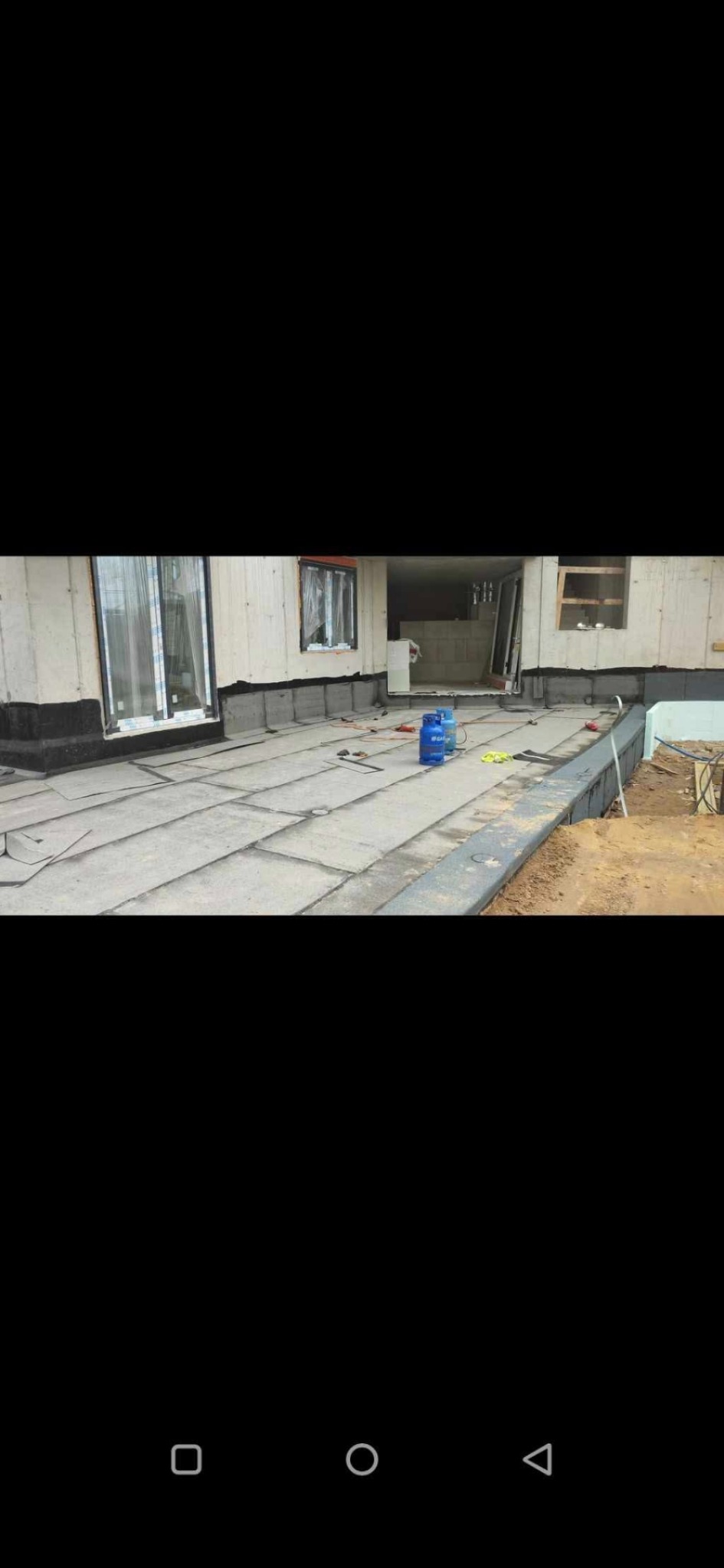 Dach budynku w trakcie krycia płytami. Widoczne narzędzia, butle gazowe, oraz elementy konstrukcji budynku. Prace dekarskie w toku.