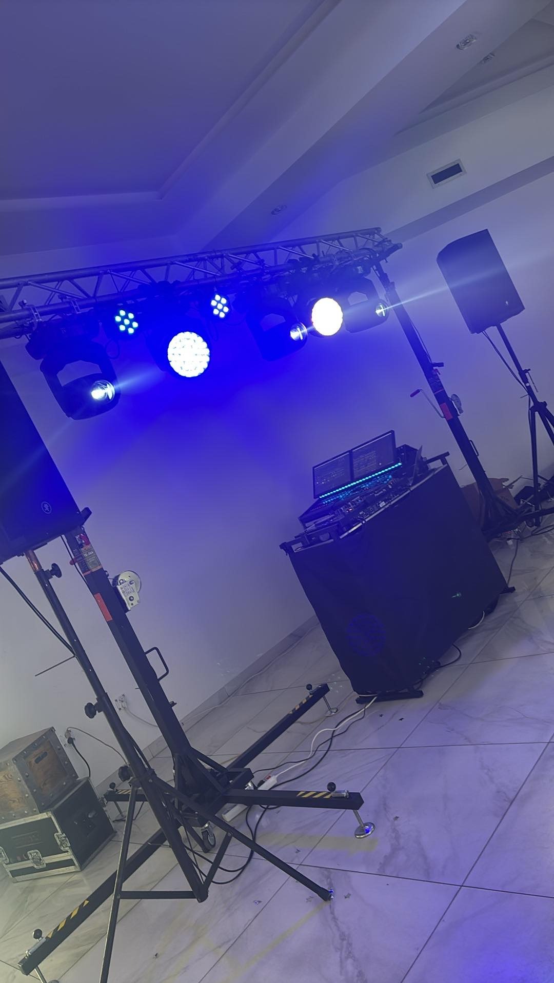 Sprzęt nagłośnieniowy i oświetleniowy z konsoletą DJ-ską na sali z białymi płytkami podłogowymi, oświetlony niebieskim światłem.