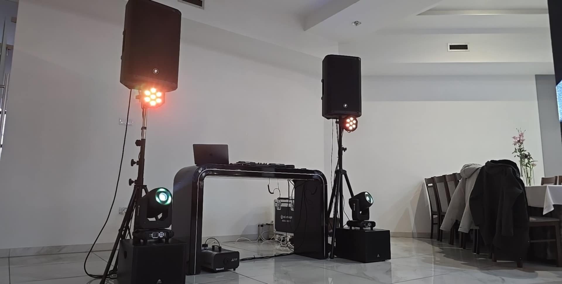 Profesjonalne nagłośnienie i oświetlenie eventowe: kolumny głośnikowe, reflektory LED i stanowisko DJ z laptopem w jasnym wnętrzu sali bankietowej.