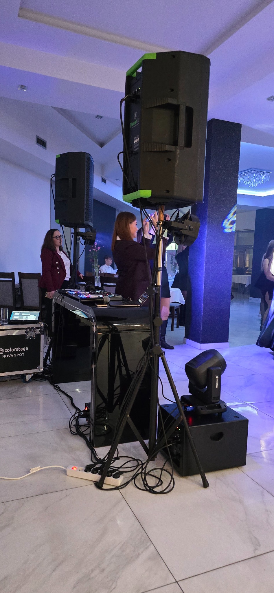 Kobiety konfigurują nagłośnienie i oświetlenie marki Colorstage Nova Spot podczas eventu w sali bankietowej z marmurową posadzką.