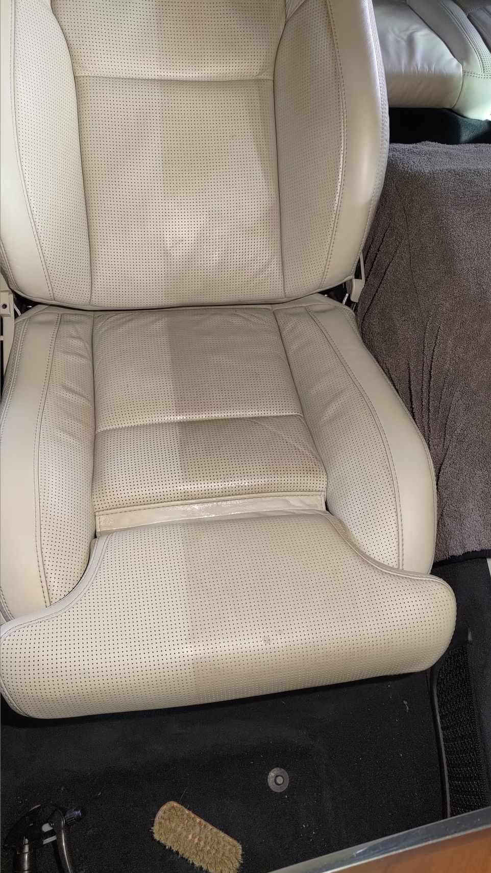 Jasna, perforowana skórzana tapicerka samochodowa po czyszczeniu, widoczna szczotka do czyszczenia. Fotel o wyraźnych śladach zabrudzeń przed zabiegiem.