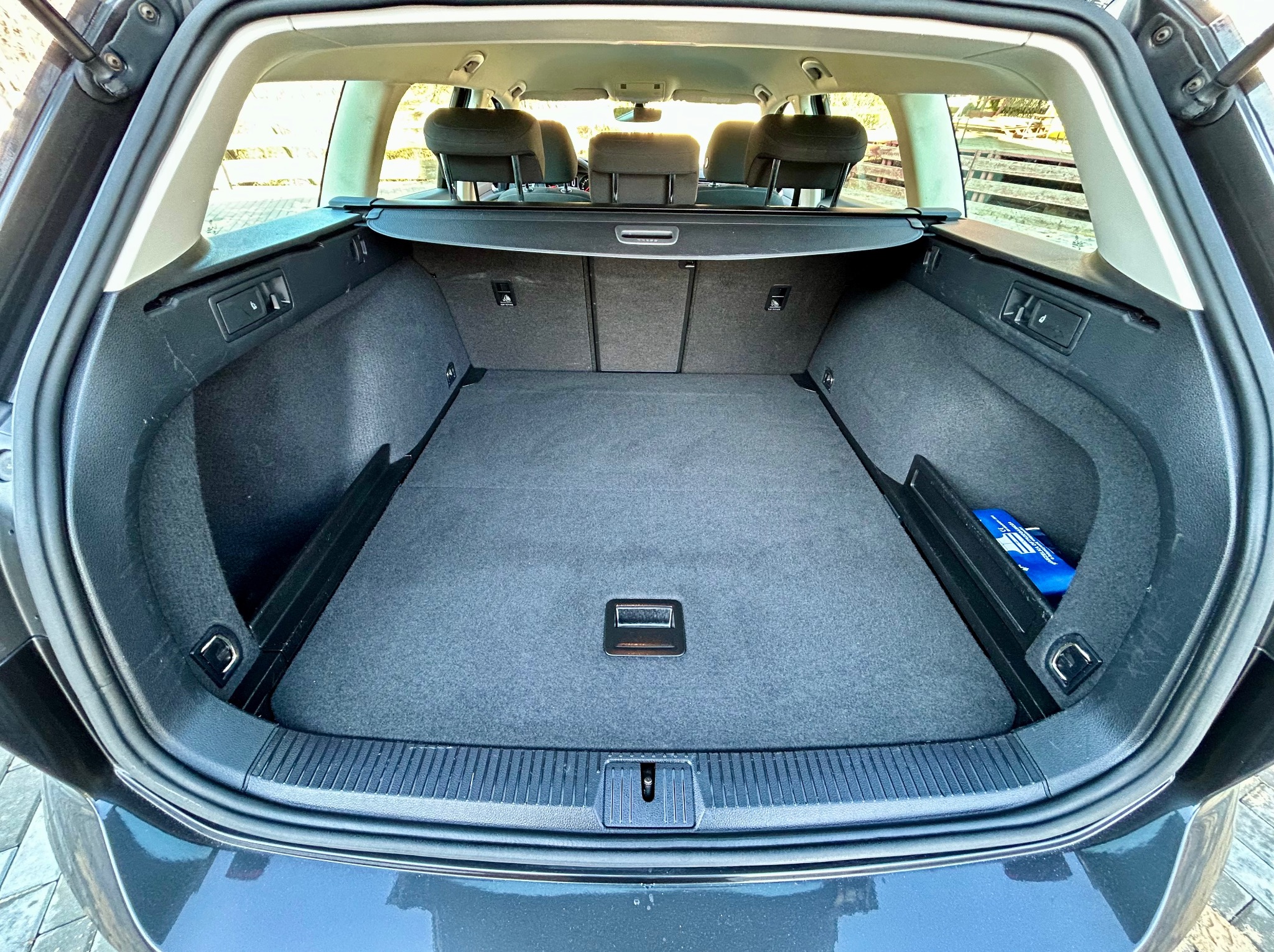 Czysty bagażnik kombi z szarą tapicerką, widok z tyłu auta, z apteczką w schowku po prawej stronie.