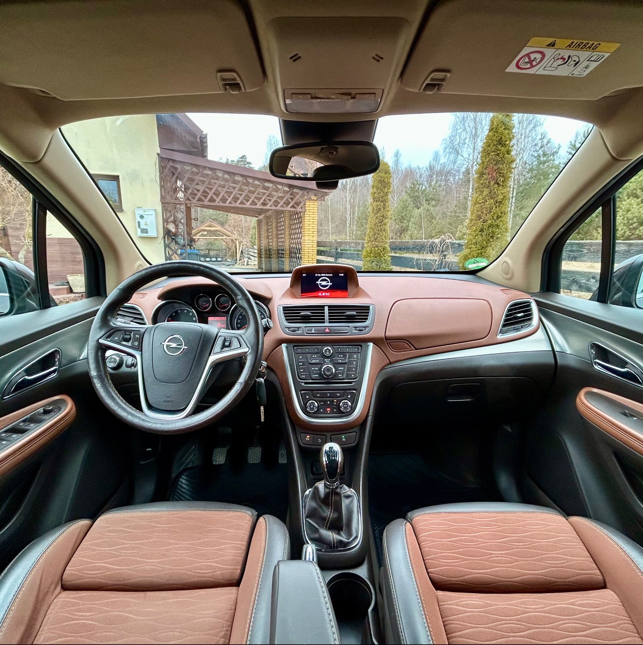 Wnętrze samochodu Opel Mokka z brązową tapicerką, widok z perspektywy kierowcy. Kokpit z ekranem nawigacji, kierownica z logo marki, fotele z wyraźną fakturą.