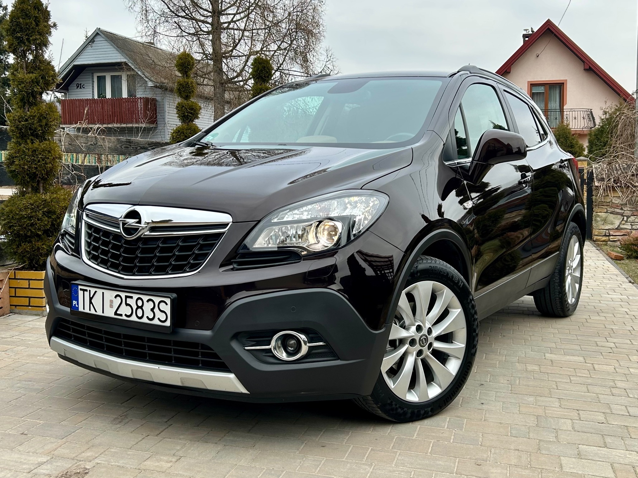 Błyszczący, ciemny Opel Mokka po myciu, zaparkowany na kostce brukowej przed domem. Widoczne detale: aluminiowe felgi, reflektory i tablica rejestracyjna.