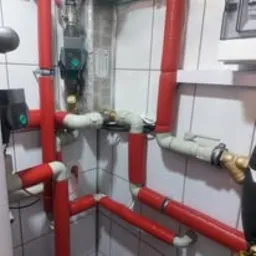 Instalacja CO z czerwonymi rurami w kotłowni wyłożonej kafelkami, widok z góry. Usługi hydrauliczne Konin.