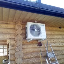 Zamontowany klimatyzator Fujitsu na drewnianej ścianie domku letniskowego, widoczna drabina i wystająca instalacja. Ujęcie z dołu, podkreślające montaż na wysokości.