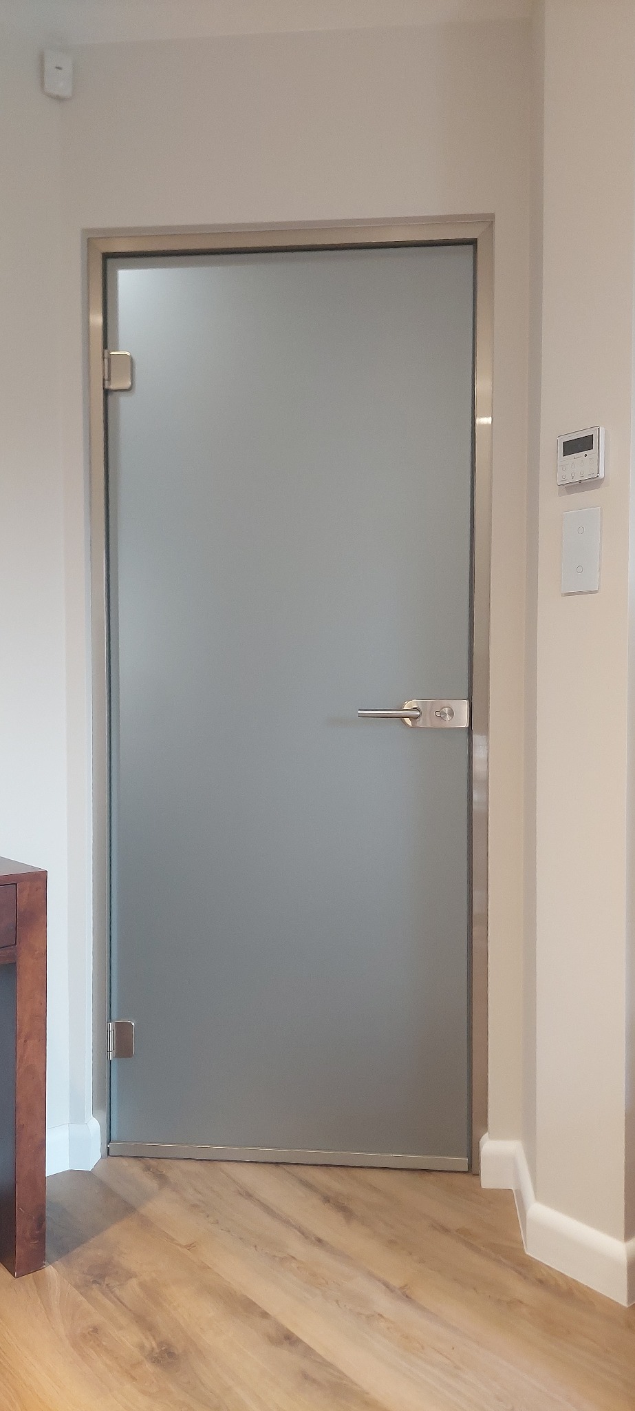 Szklane drzwi z satynowym wykończeniem i metalową ramą, zamontowane w nowoczesnym wnętrzu w Warszawie. Minimalistyczny design, widoczne zawiasy.