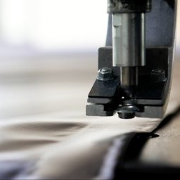 BANNERPRINT SPÓŁKA Z OGRANICZONĄ ODPOWIEDZIALNOŚCIĄ - Metalowa maszyna z nitownicą aplikuje metalowe oczko na tkaninę w jasnym kolorze.