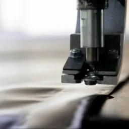 Metalowa maszyna z nitownicą aplikuje metalowe oczko na tkaninę w jasnym kolorze.