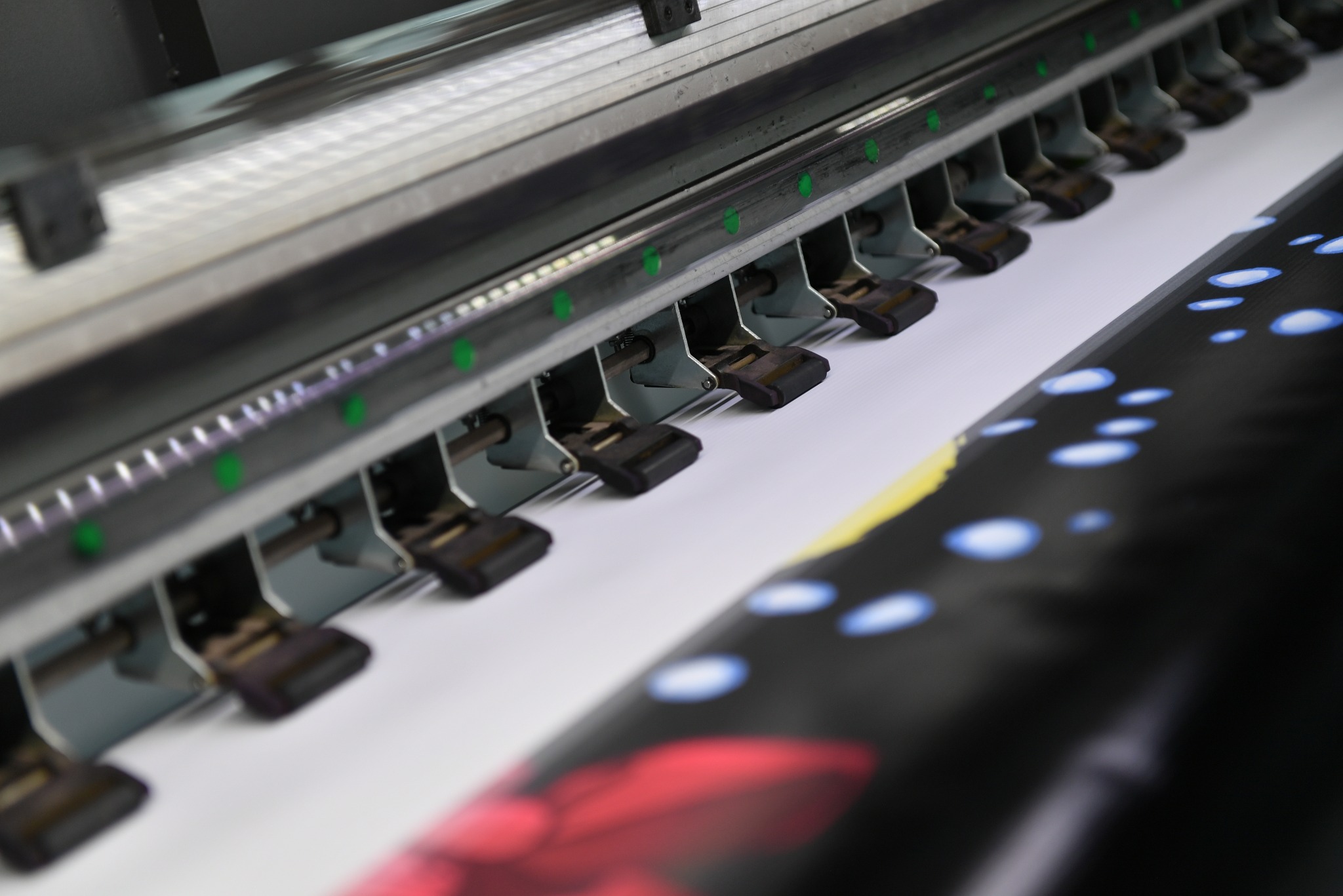 Drukarka wielkoformatowa w trakcie pracy, widoczne głowice drukujące nad zadrukowywanym materiałem z kolorowym wzorem.