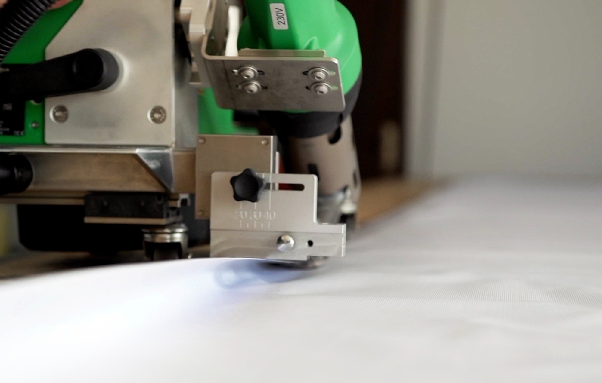 Automatyczny ploter tnący z zielonym elementem obudowy, przecinający biały, teksturowany materiał.