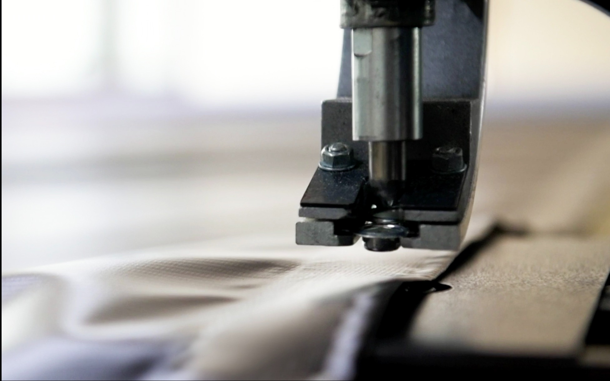 Metalowa maszyna z nitownicą aplikuje metalowe oczko na tkaninę w jasnym kolorze.